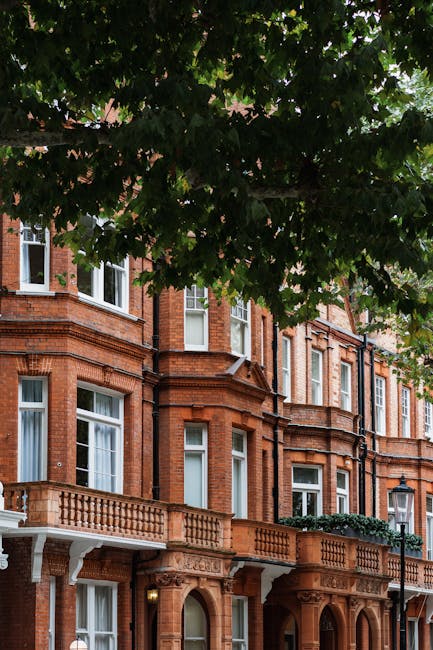 The image depicts the exterior of a multi-story residential building constructed with yellow brickwork, featuring large white-framed sash windows with decorative molding. The roof is pitched and cover
